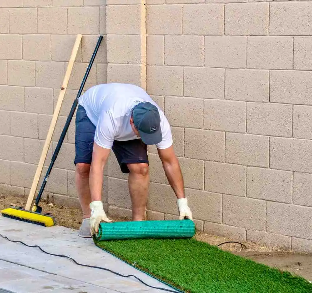 How to Install Synthetic Turf Grass by rolling out artificial grass over a prepared base during DIY synthetic grass installation